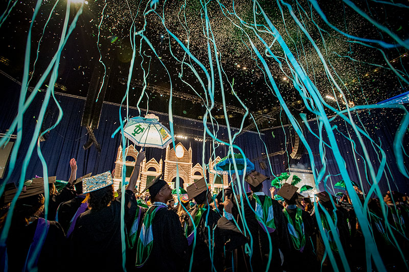 Graduates in caps and gowns throw blue streamers in the air.