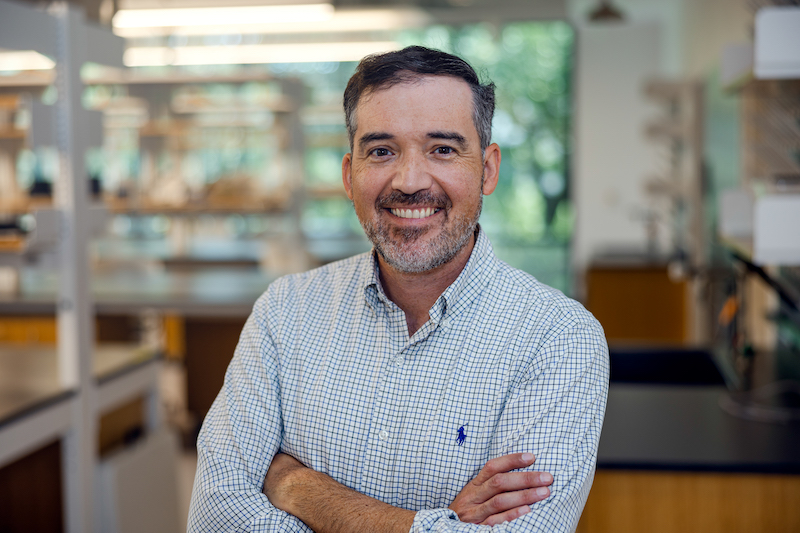 Man with arms crossed, smiling, in a lab coat.