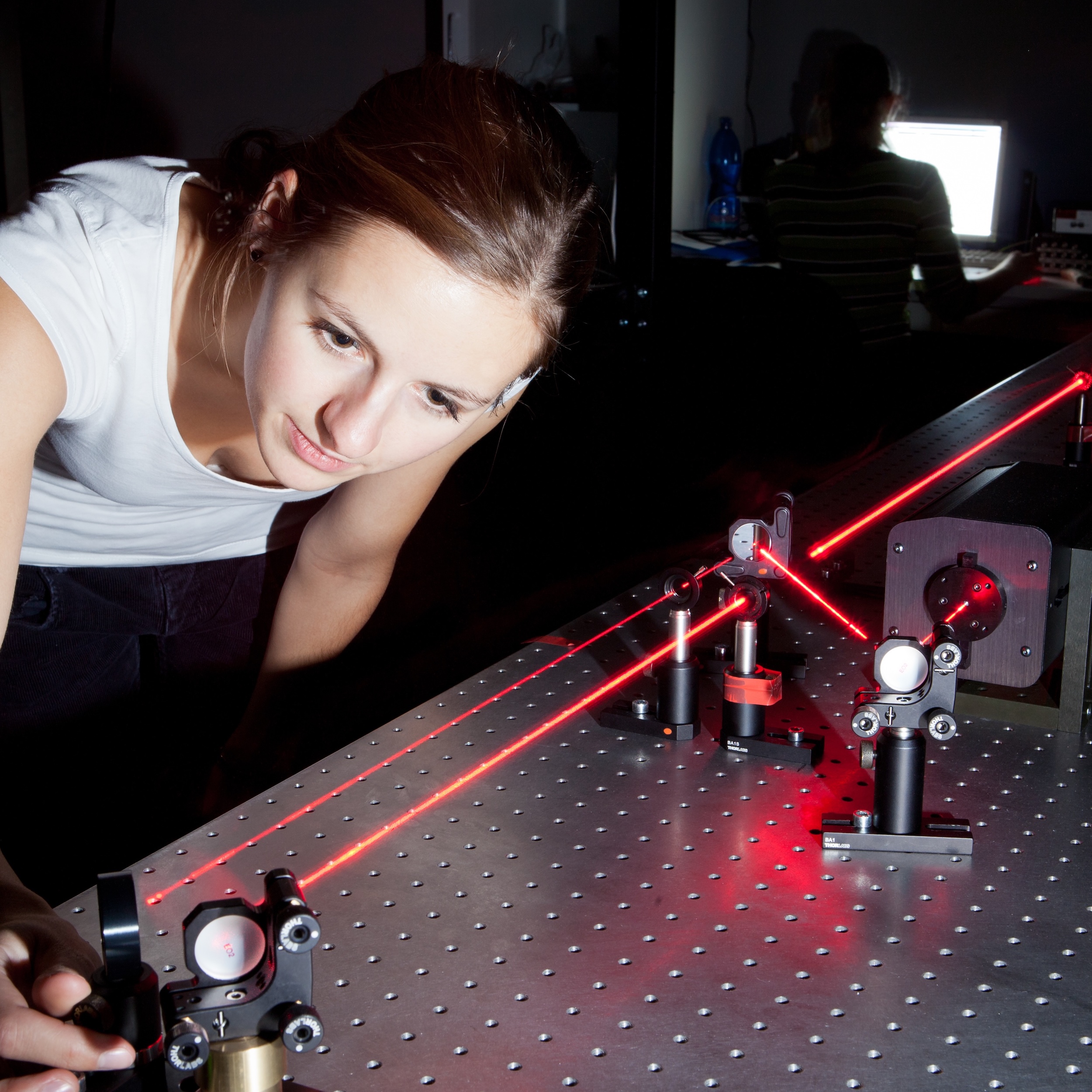 Woman adjusts optical experiment with red lasers.