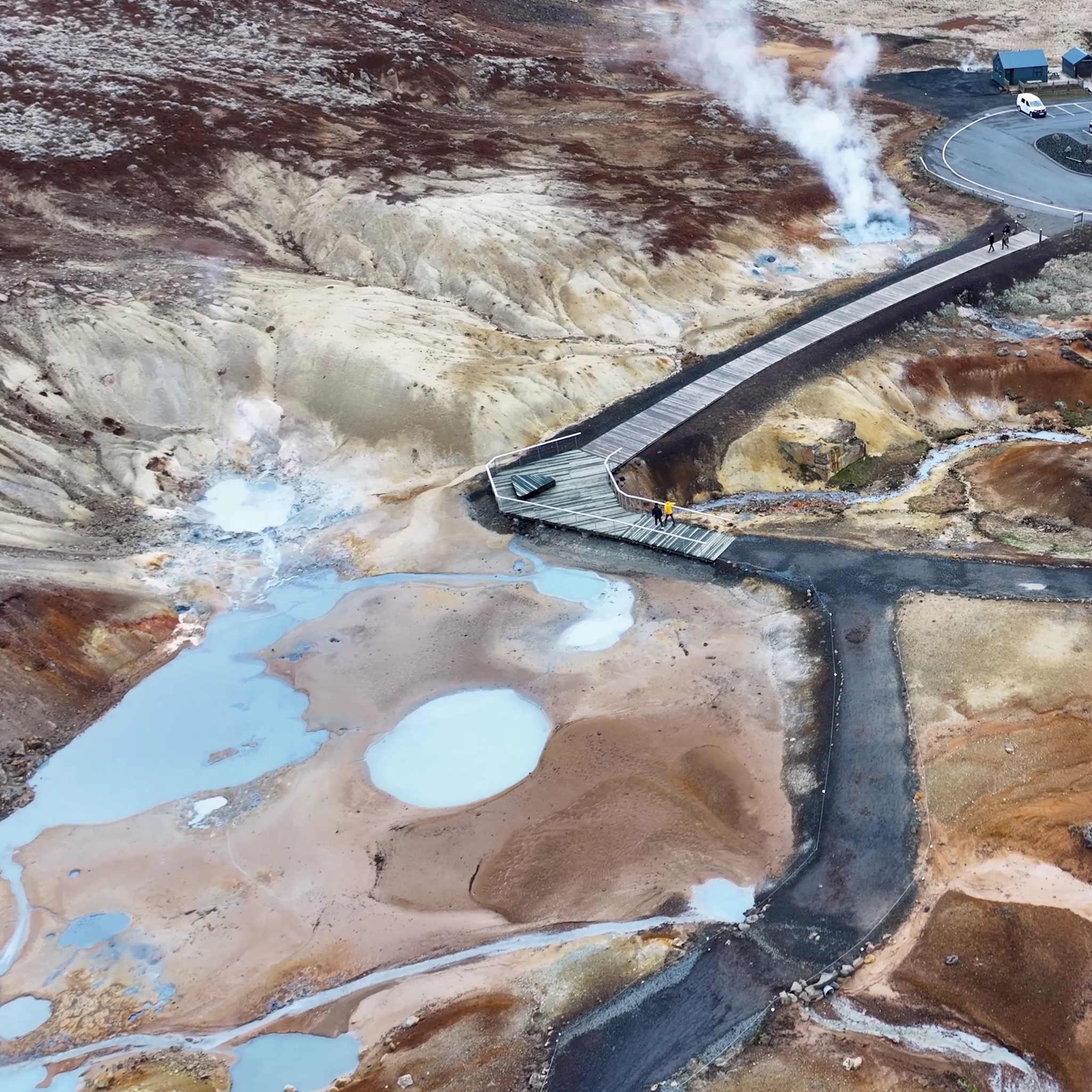 Aerial view of a geothermal area with steaming vents and blue pools.