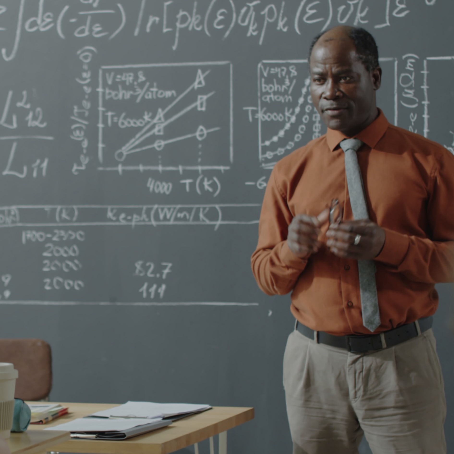 professor-pointing-at-graphs-and-formulas-on-blackboard