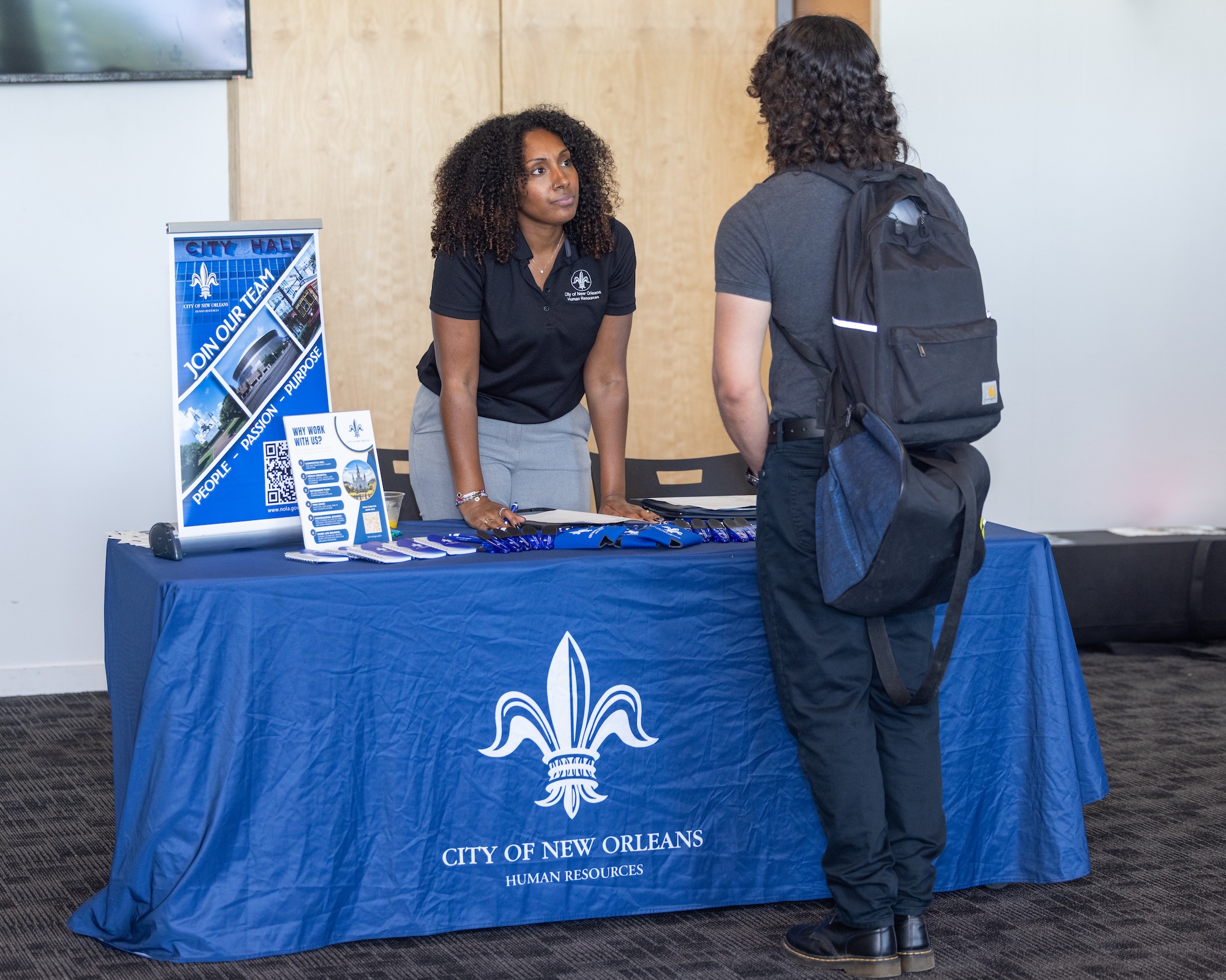 Woman at a City of New Orleans table talks to a person with a backpack.