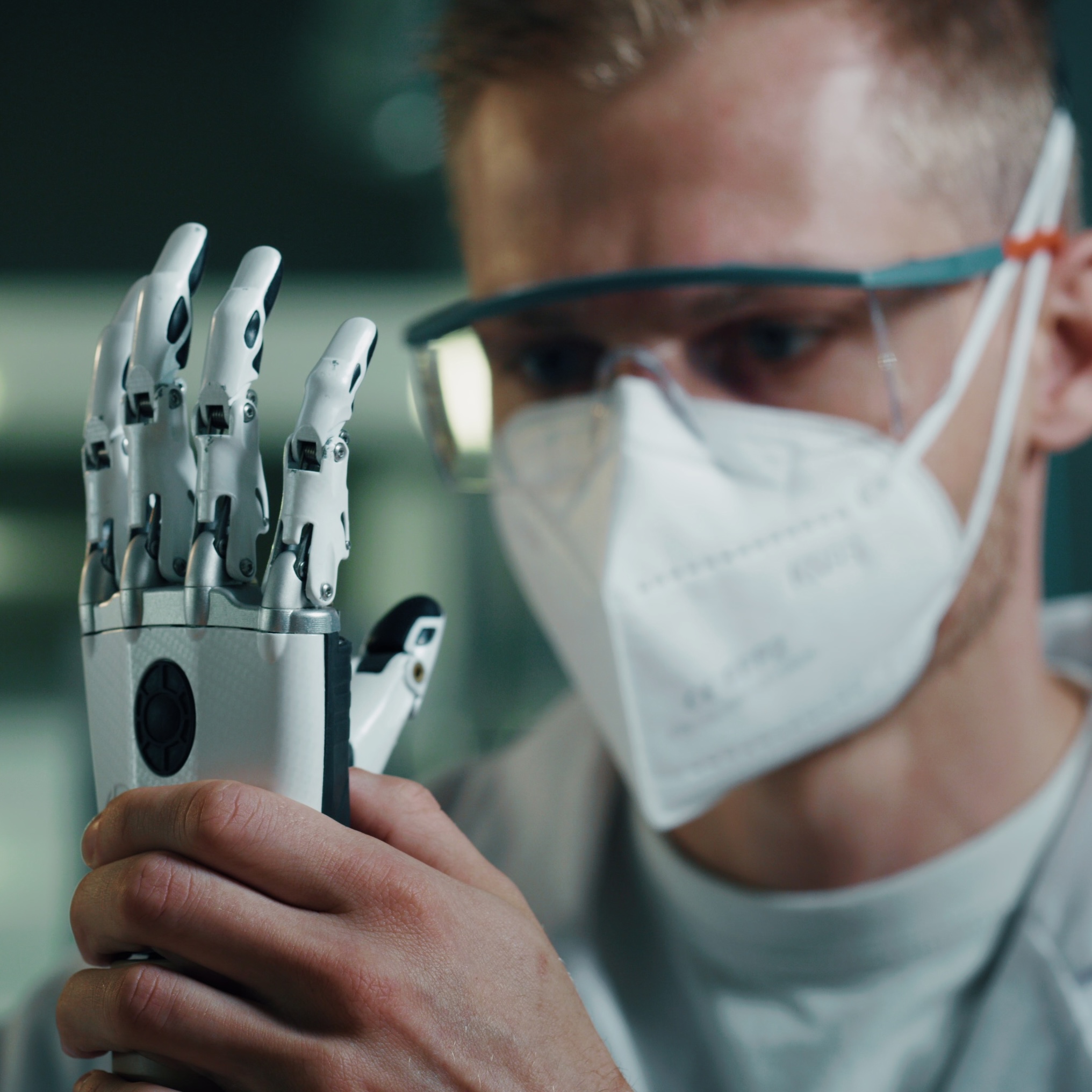 Man in mask and goggles holds prosthetic hand.
