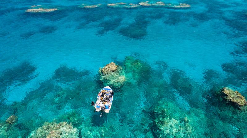 Small boat drifting over a vibrant coral reef.