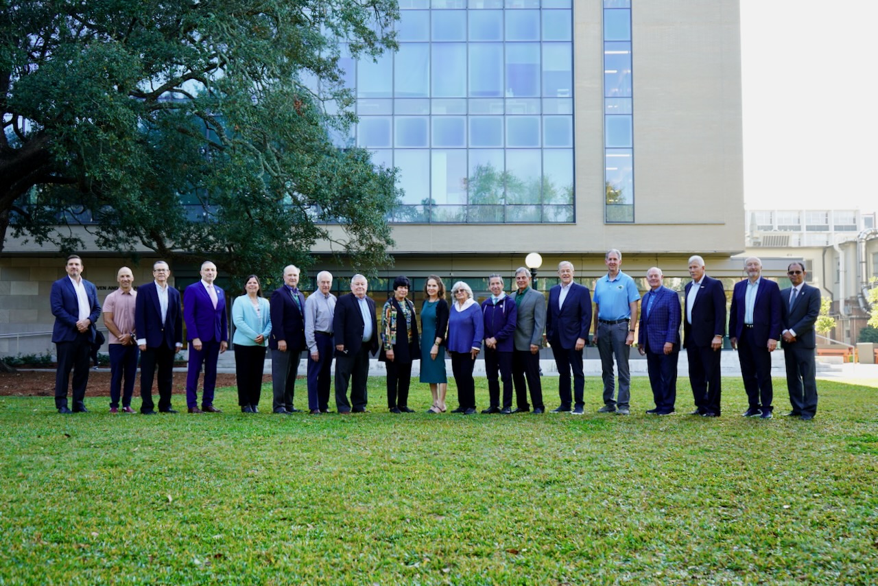 Group of people in professional attire standing on a lawn in front of a building.