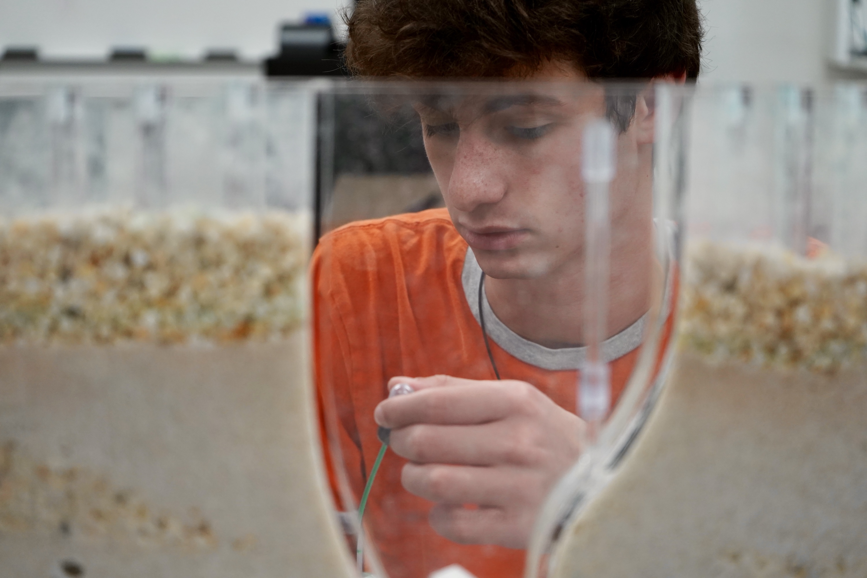 Young man in orange shirt conducts experiment in lab.