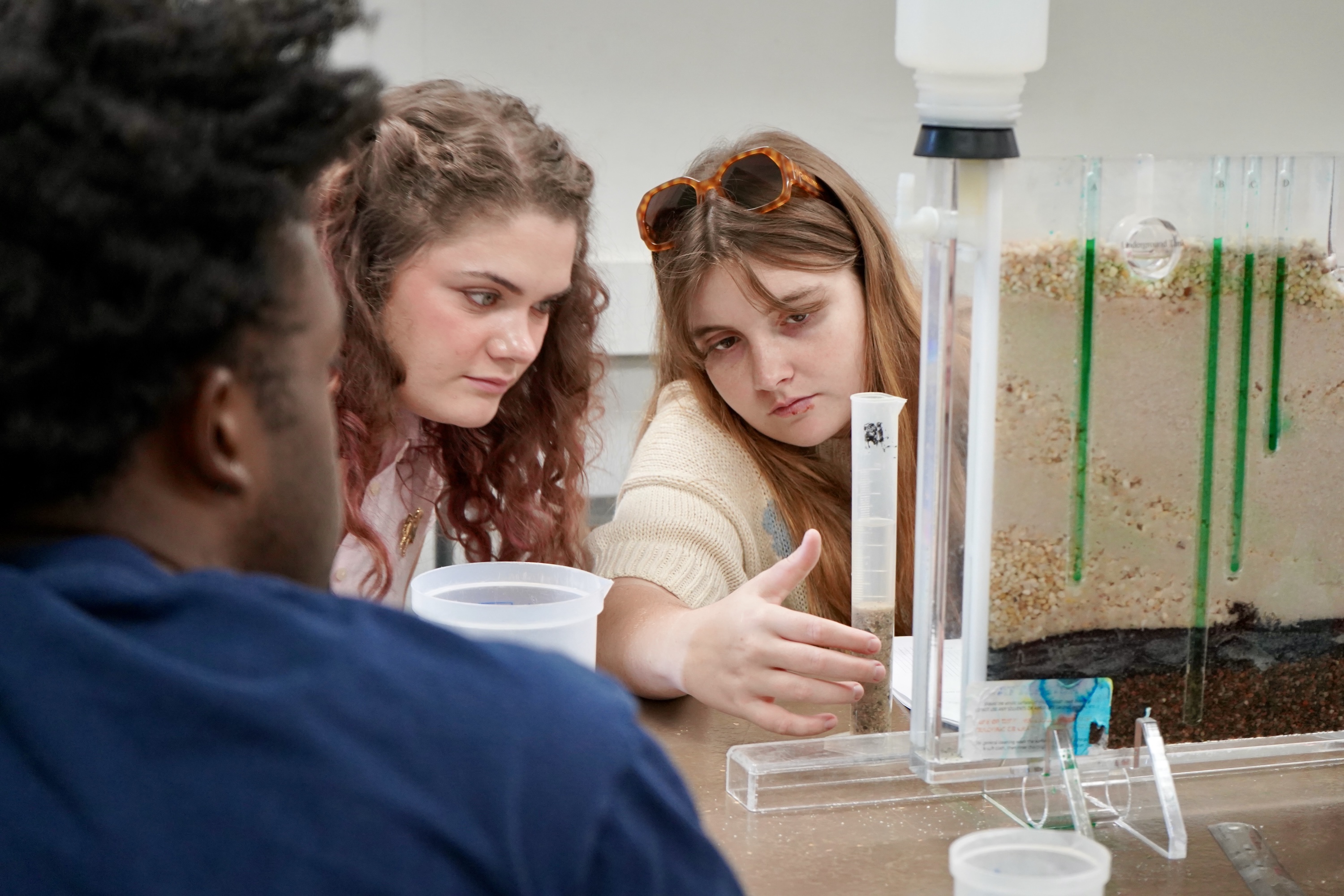 Three students observe a science experiment with a clear tank.