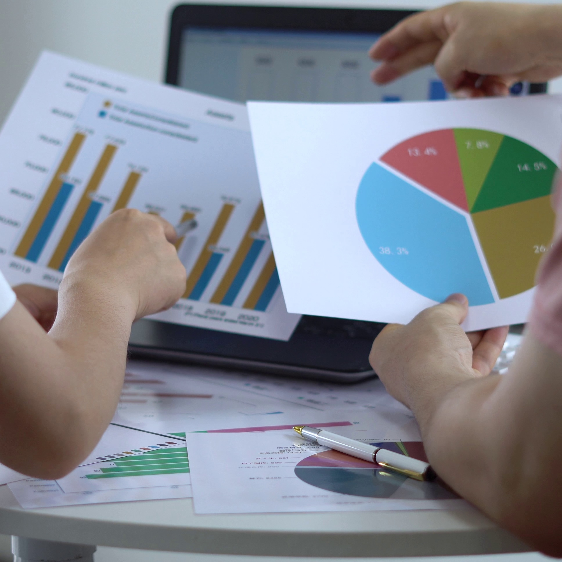 Hands reviewing bar and pie charts on a desk with laptop.