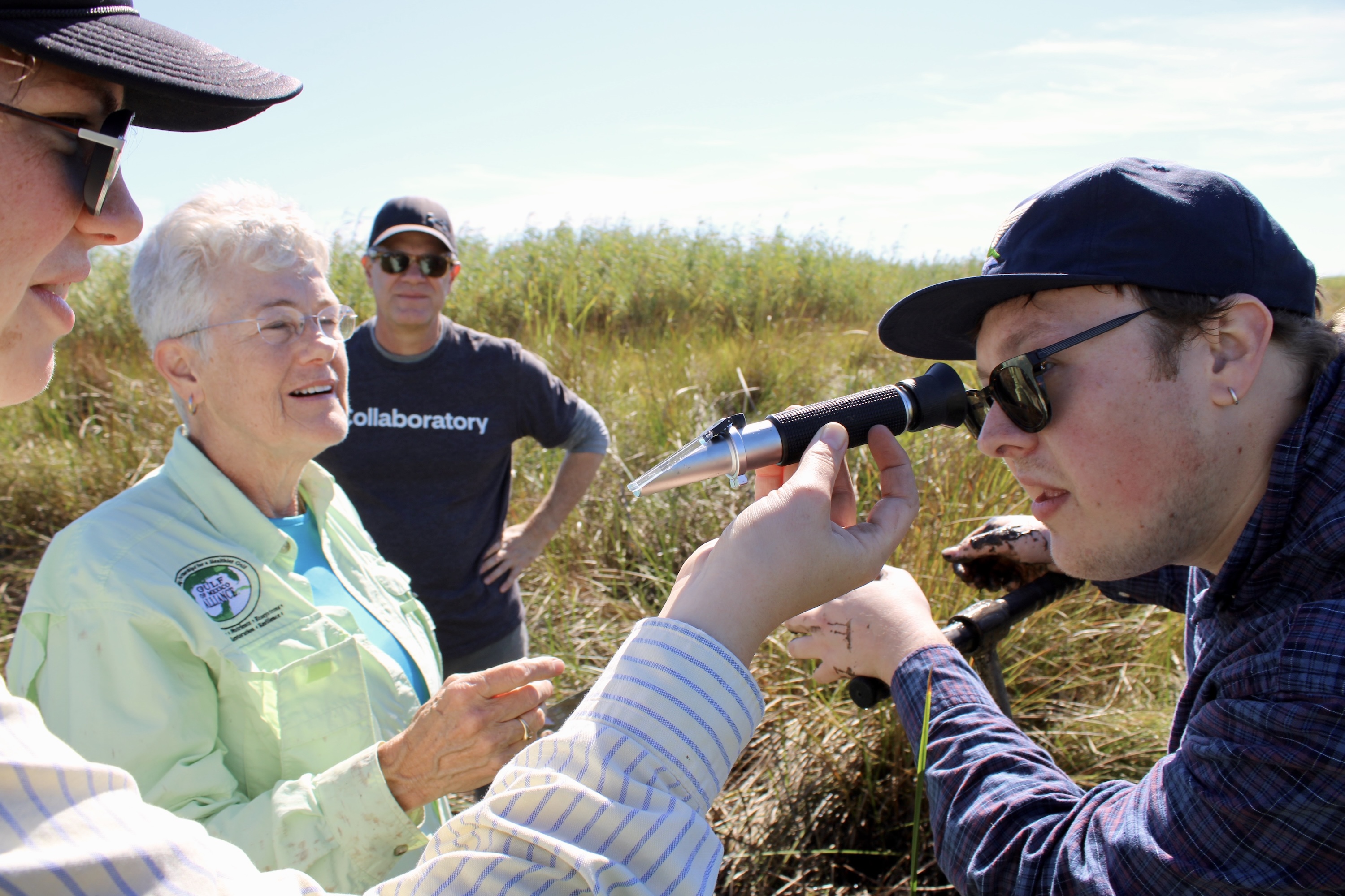 Young person uses refractometer to test water, with adults watching.