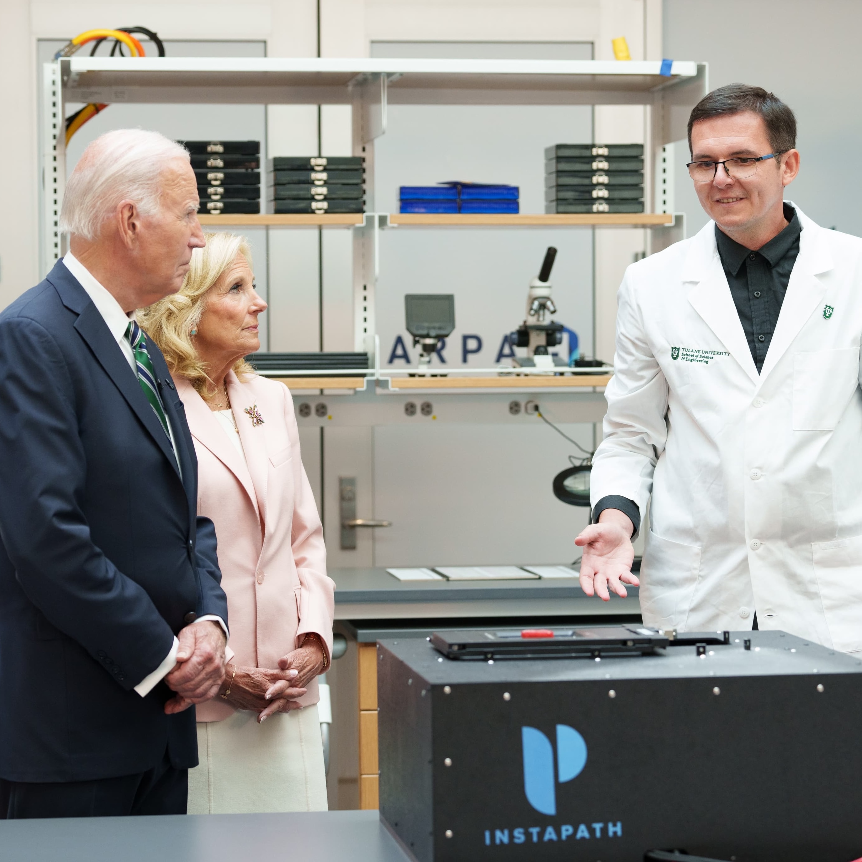 President Biden and Jill Biden listen to a scientist in a lab.