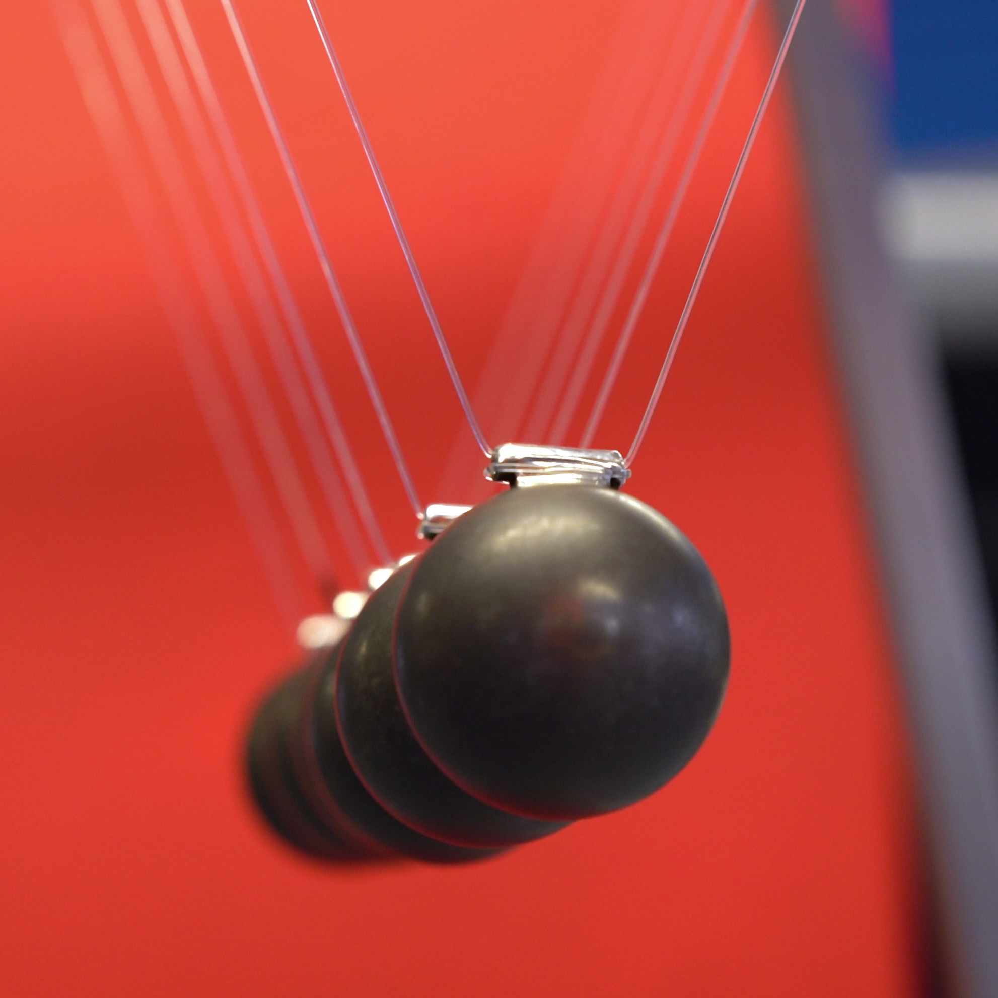 Newton's cradle with black spheres against a red background.