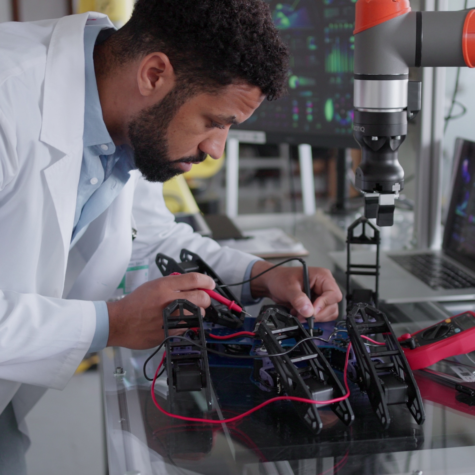 Man in lab coat works on robotic arm components.