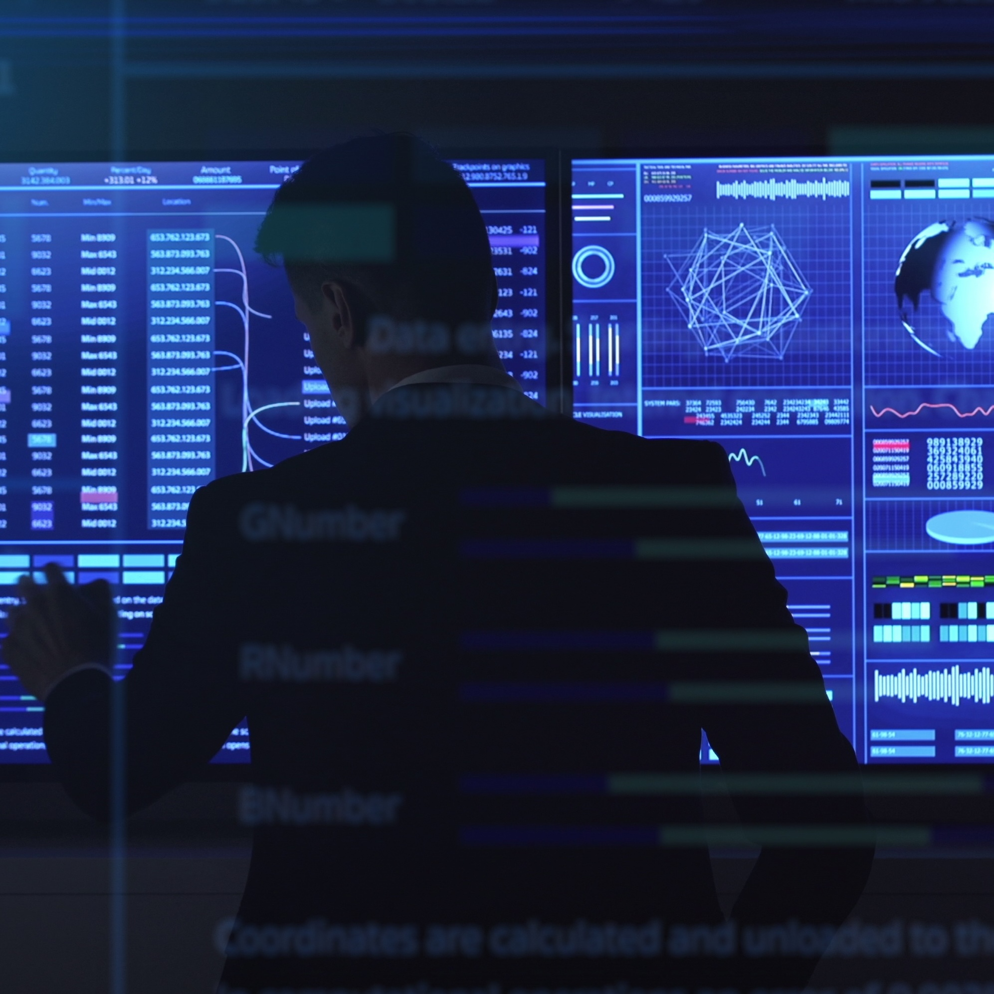 Man in suit pointing at complex data visualization screens.