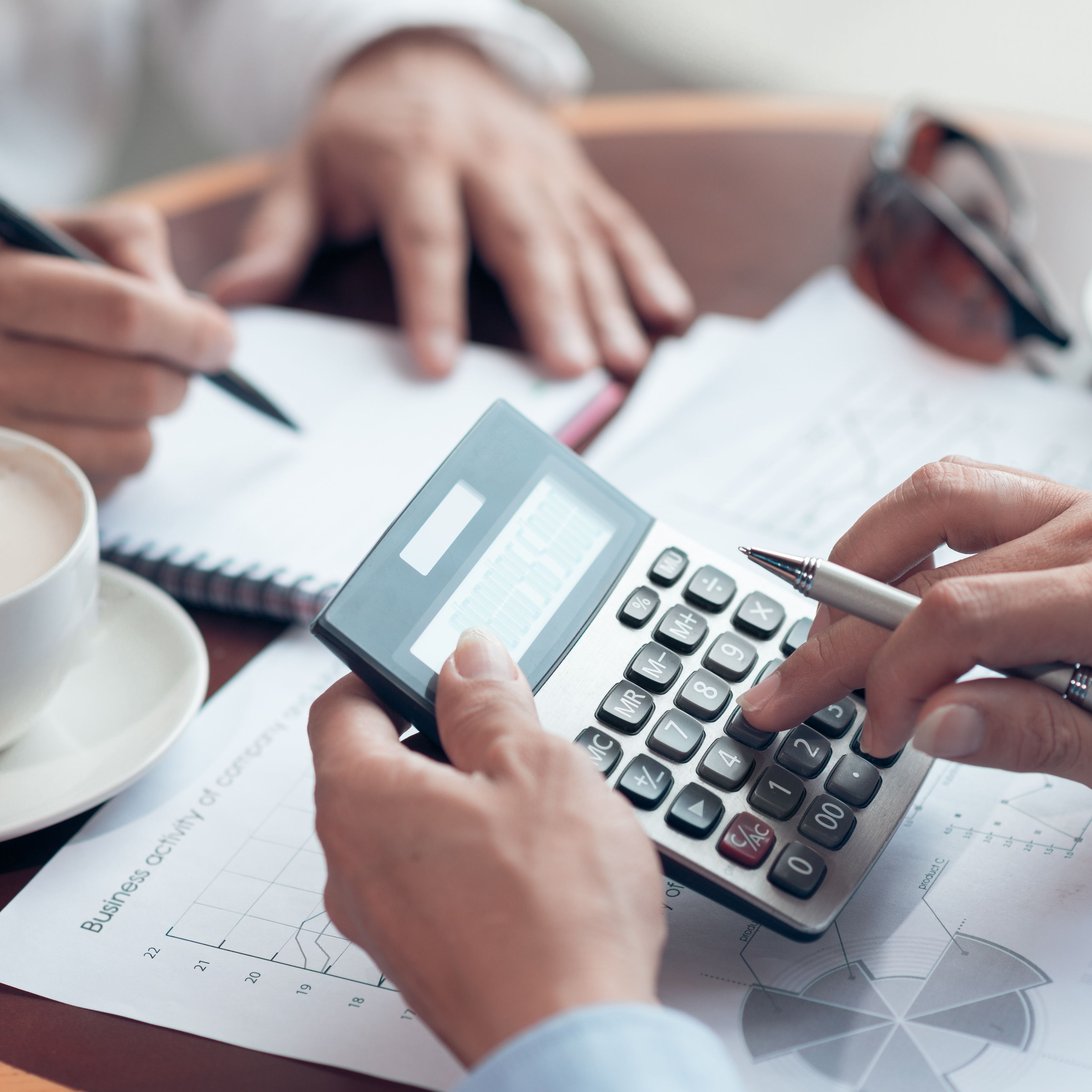 Hands using a calculator and pen over financial documents and a notebook.