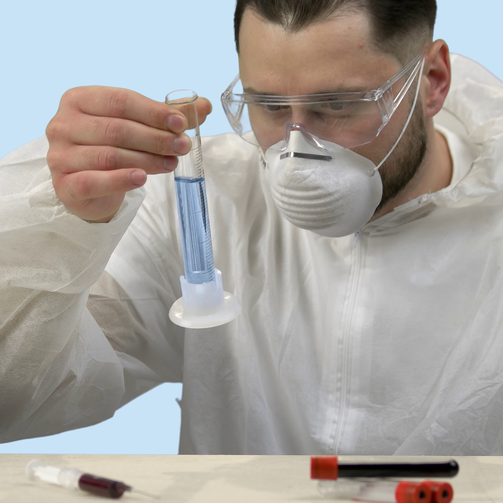 Scientist in protective gear examines blue liquid in a test tube.