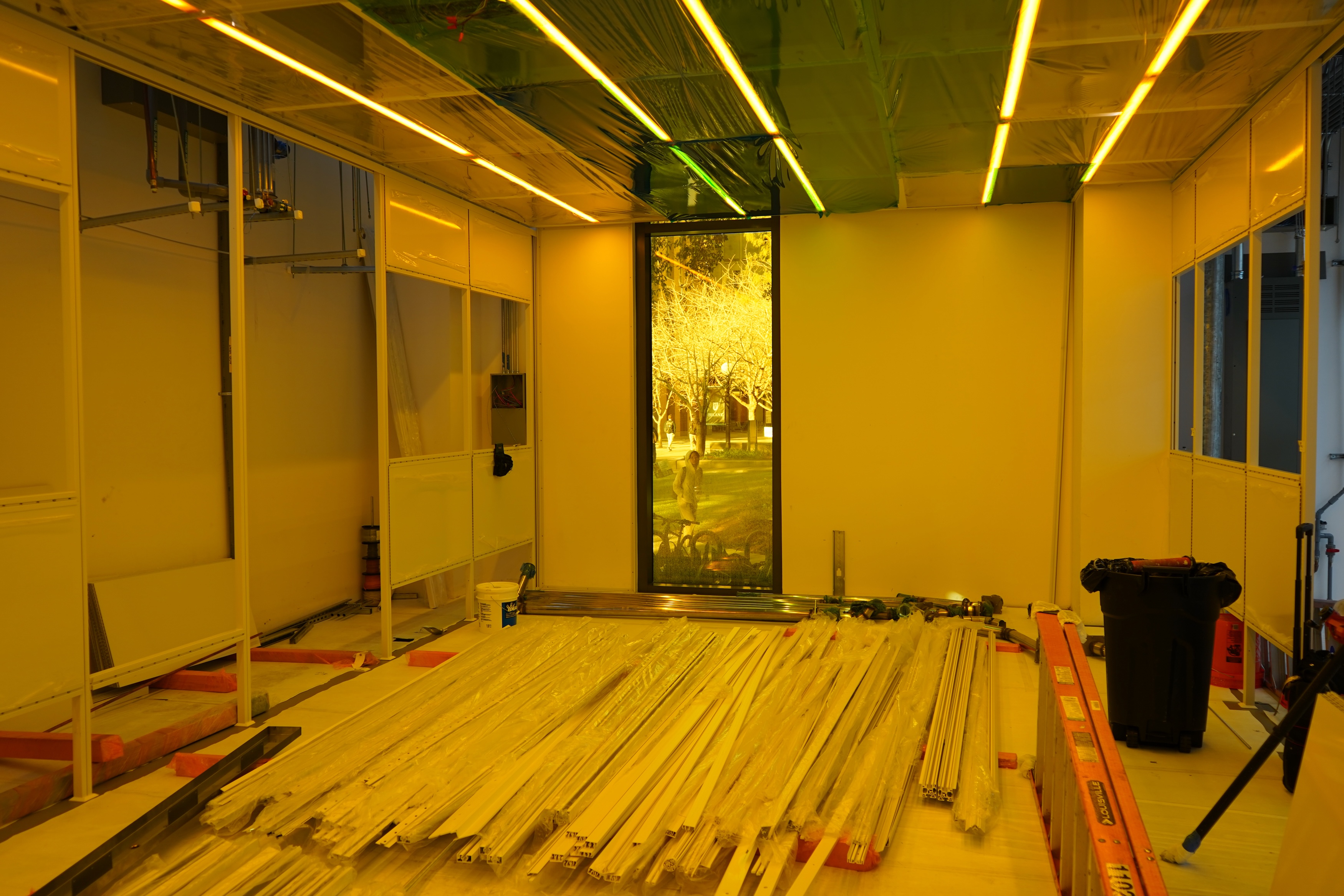 A room with bright yellow walls, a floor covered in wood planks, and a large vertical screen displaying a park scene.