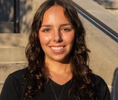 Young woman with dark curly hair and a black shirt smiles.