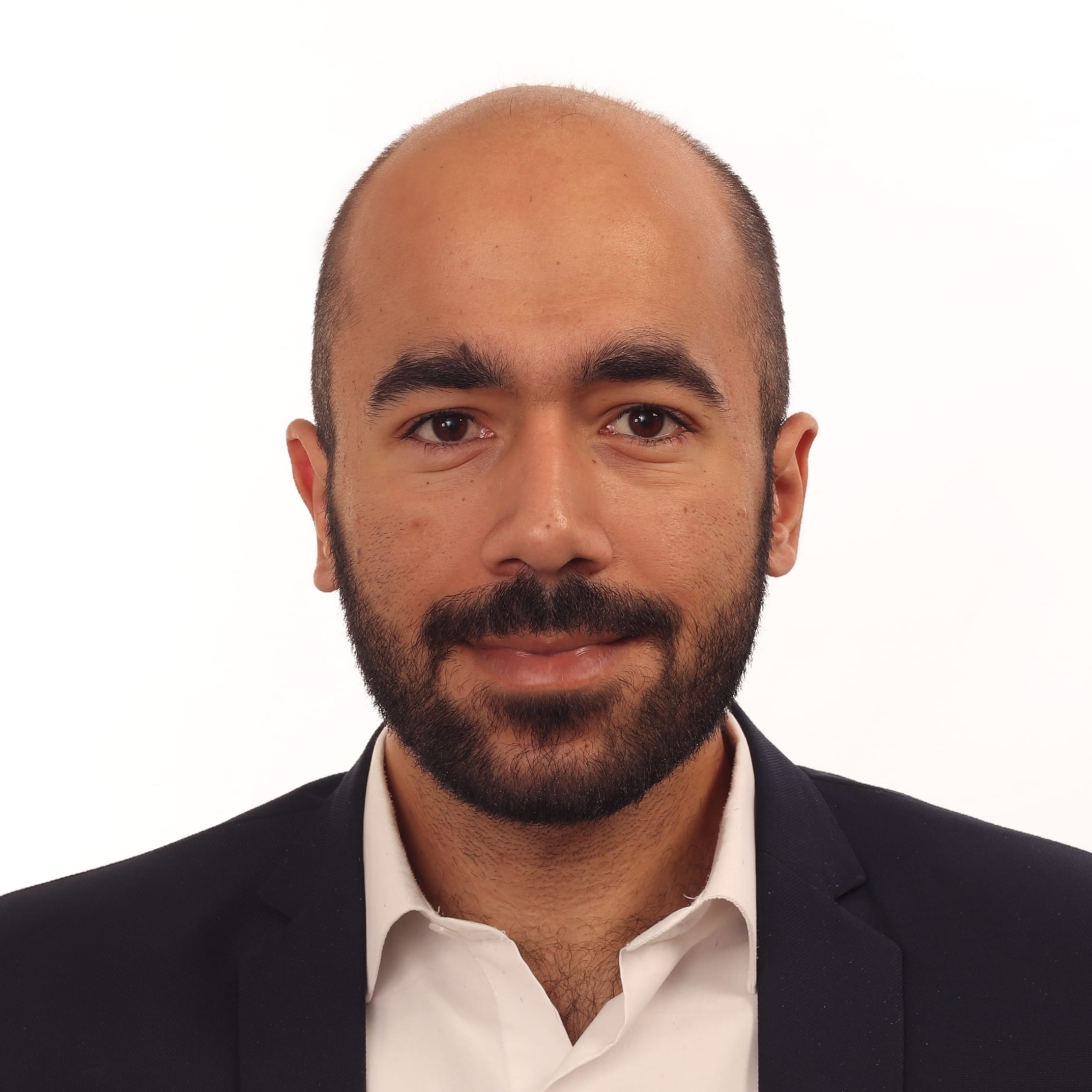 Headshot of a smiling man with a beard wearing a dark suit and white shirt.