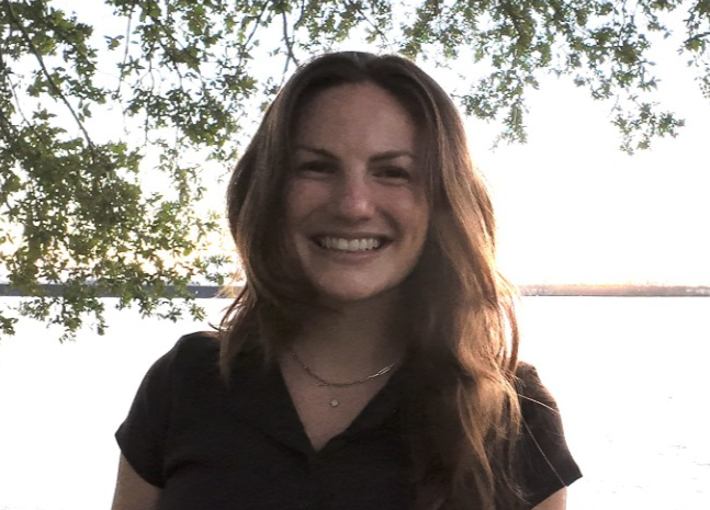 Young woman smiles at camera, with trees and water in background.