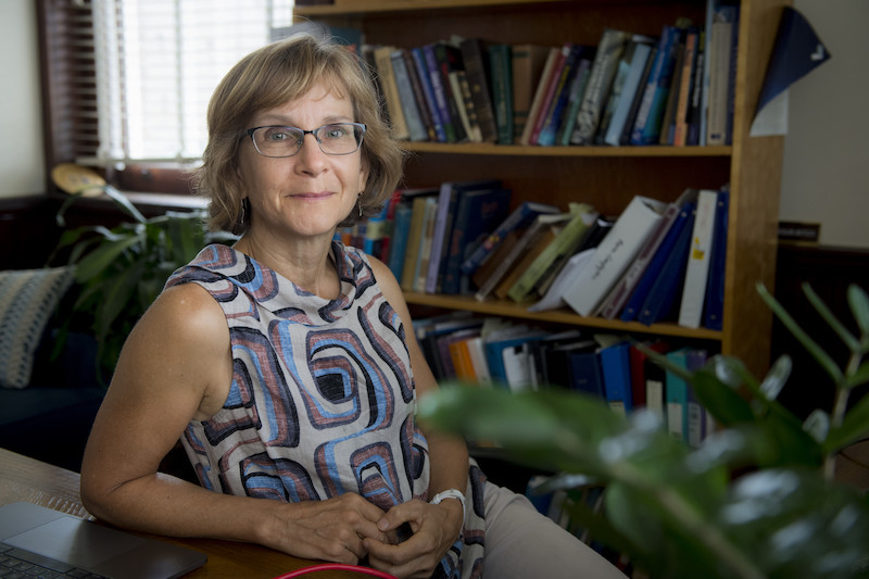 Woman with glasses in front of a bookshelf.