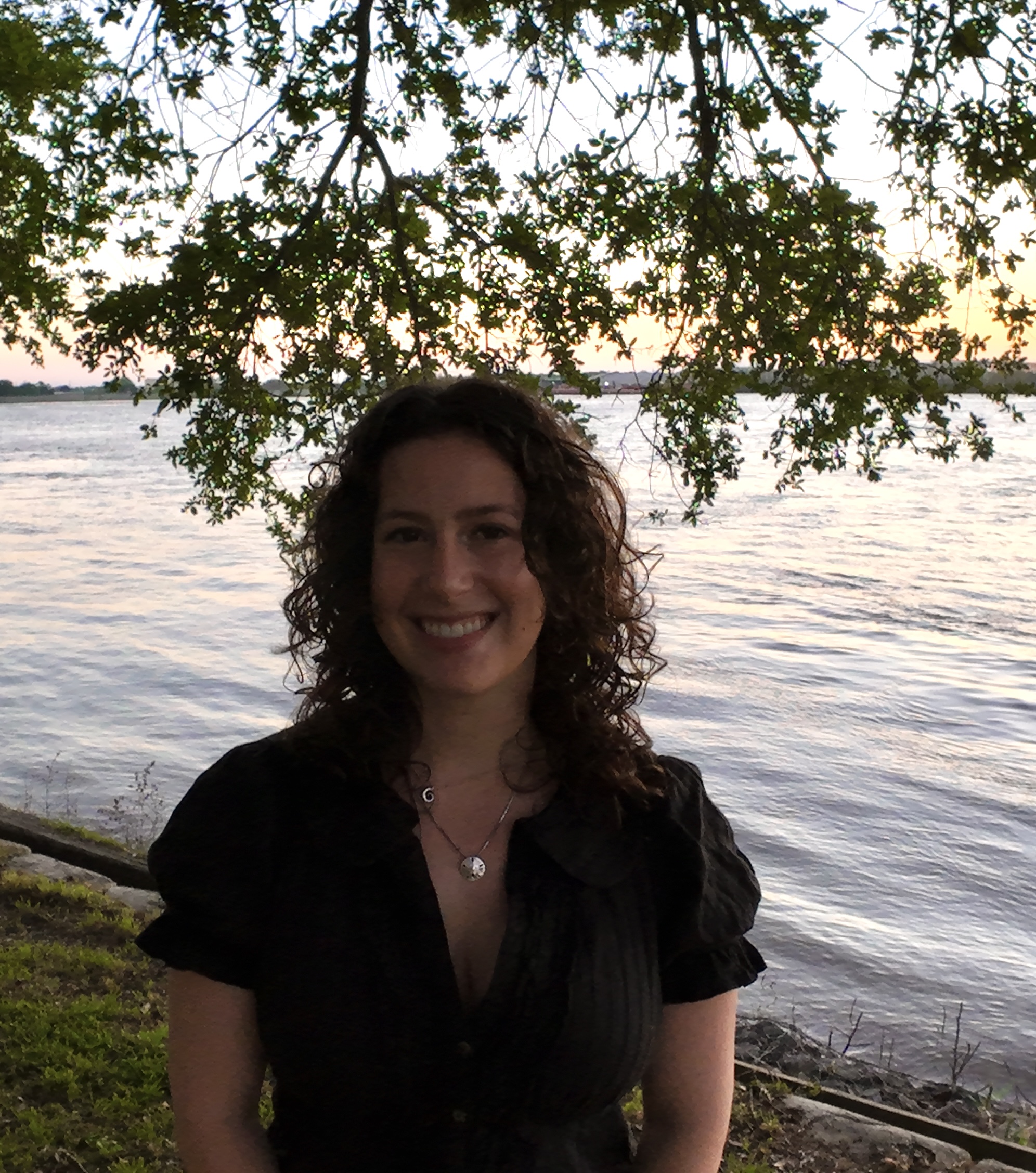 Smiling woman with curly hair in a black top by the water.