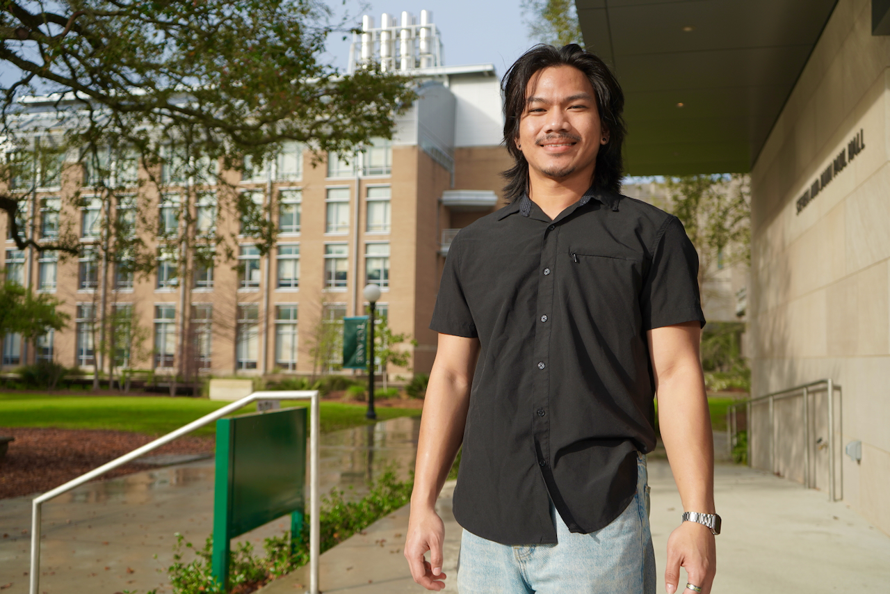 Young man in a black shirt smiles on a campus.