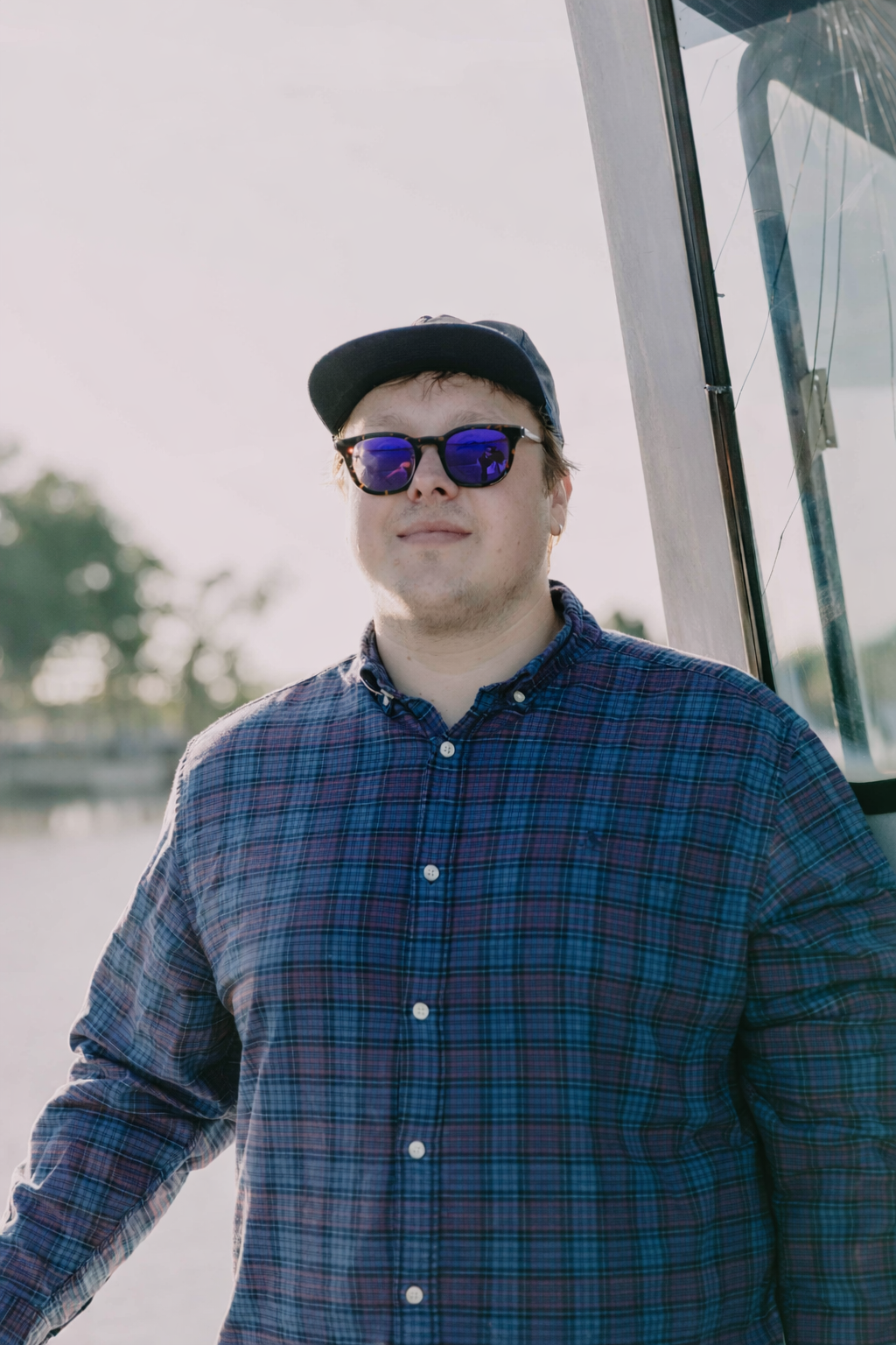 Man in plaid shirt, sunglasses, and baseball cap on a boat.