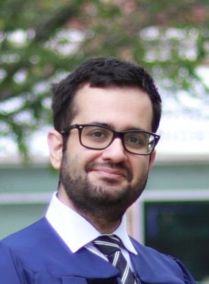 Man in graduation gown and cap, wearing glasses, smiling.