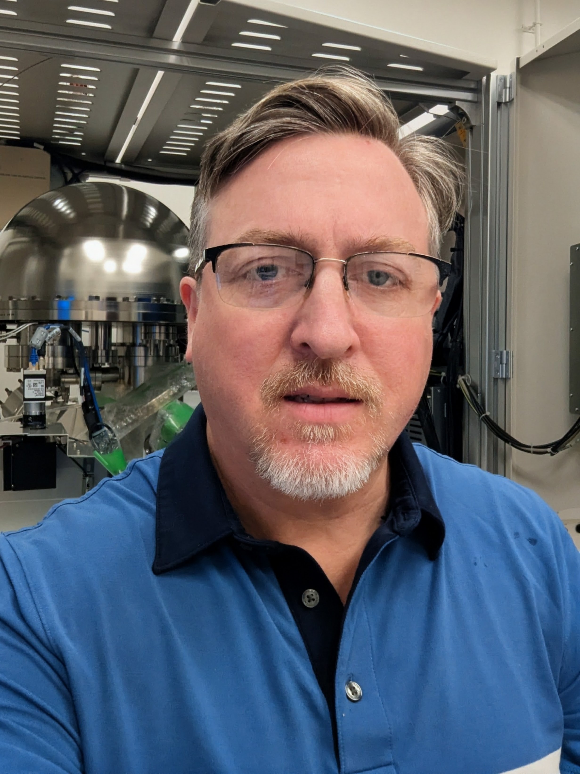Man wearing glasses and a blue polo shirt in a laboratory.