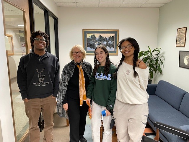Four people stand together in a hallway, smiling.