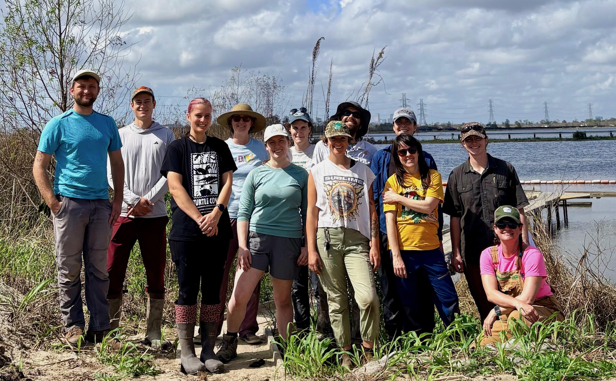 Group of people posing for a photo outdoors by the water.