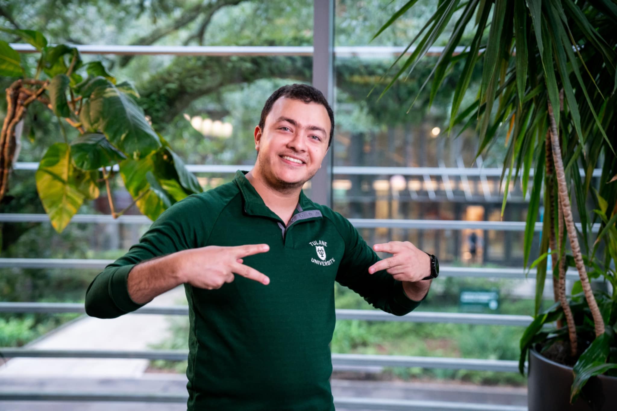 Man in green polo shirt flashes peace signs between plants.