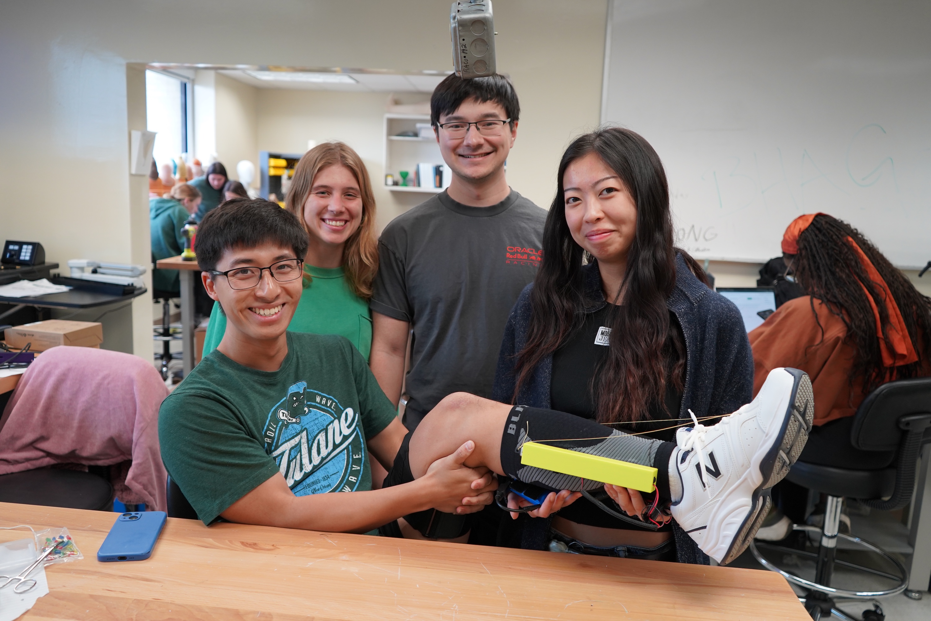 Four smiling young adults in a lab, one holding a prosthetic leg.