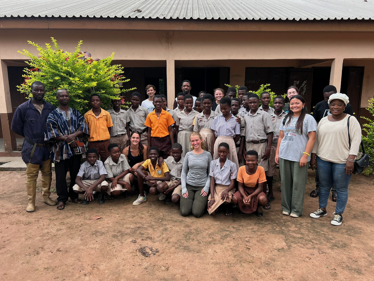 Group of students and adults pose for a photo outside a building.