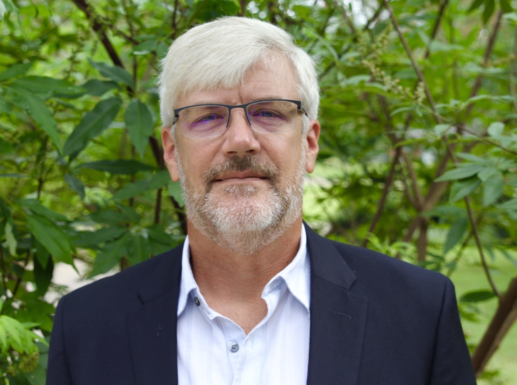 Photograph of a middle-aged man with grey hair and glasses, wearing a suit jacket.