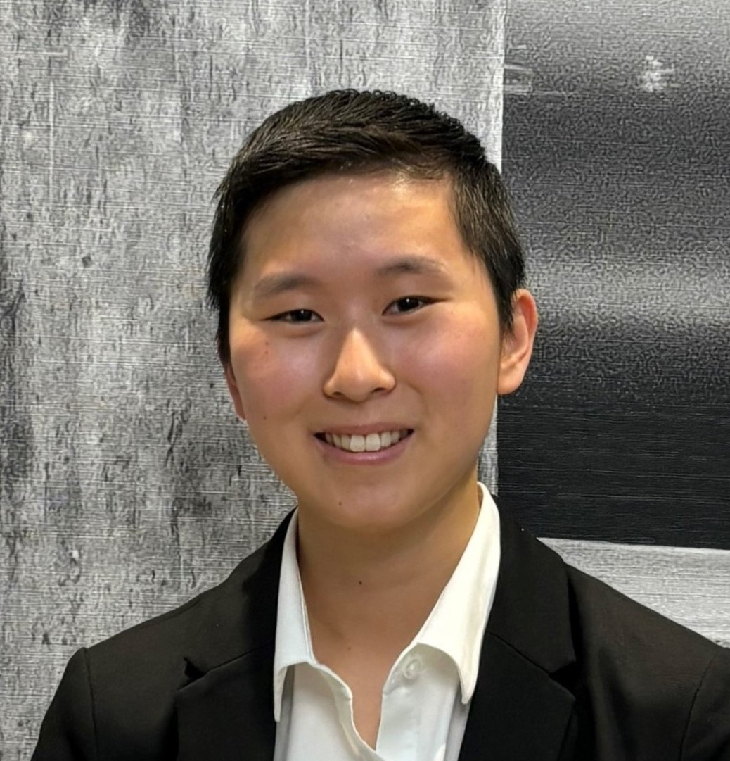 Portrait of a young Asian person with short hair, wearing a black suit jacket and white shirt, smiling.