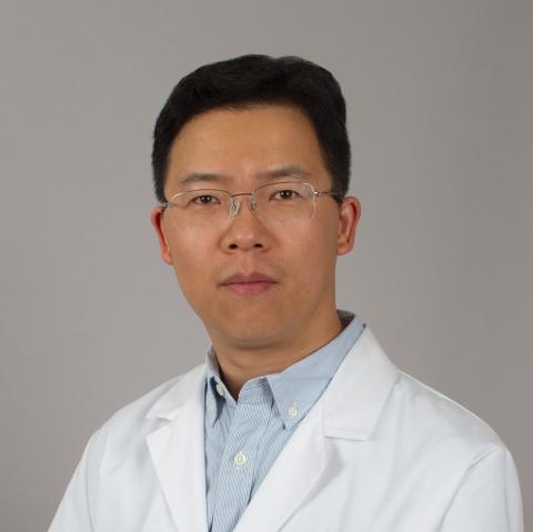 A man in a lab coat wearing glasses, looking forward.