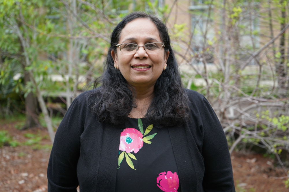 Professor Meena Vijayaraghavan standing in front of trees