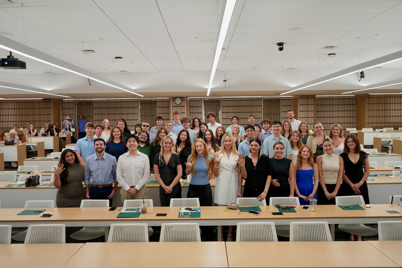 A large group of diverse young adults posing for a photo in a modern classroom.