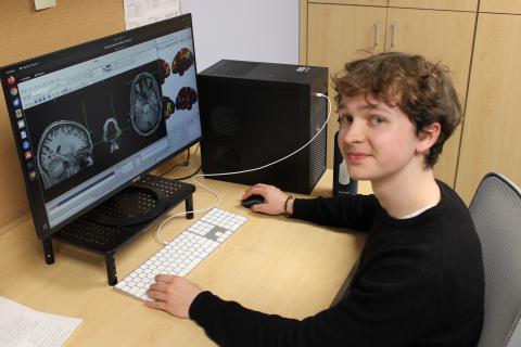 Student at a desk with a computer displaying brain scans.