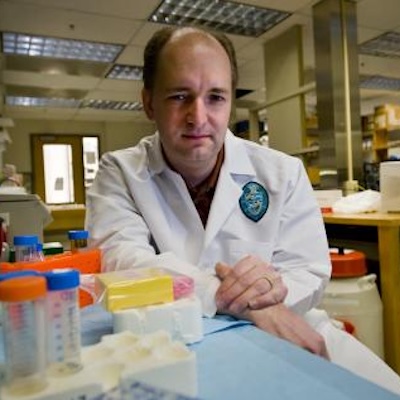 Man in lab coat with hands folded staring at camera
