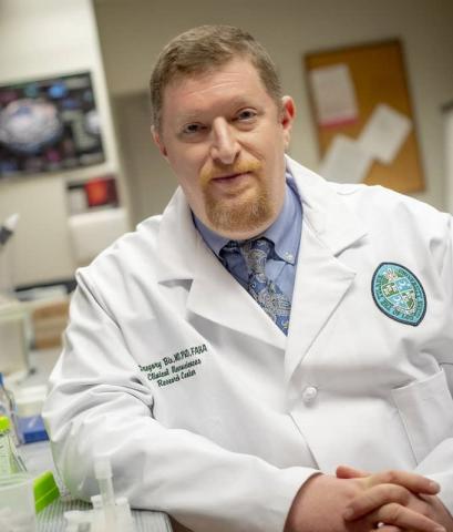 Man in lab coat with hands folded staring at camera