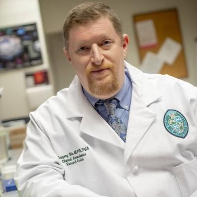 Man in lab coat with hands folded staring at camera