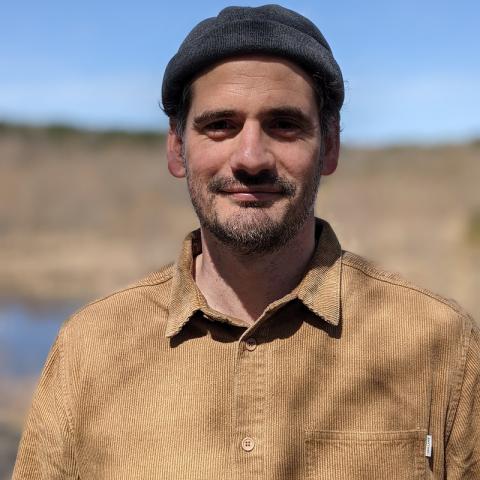 Man in beanie and corduroy shirt smiles outdoors
