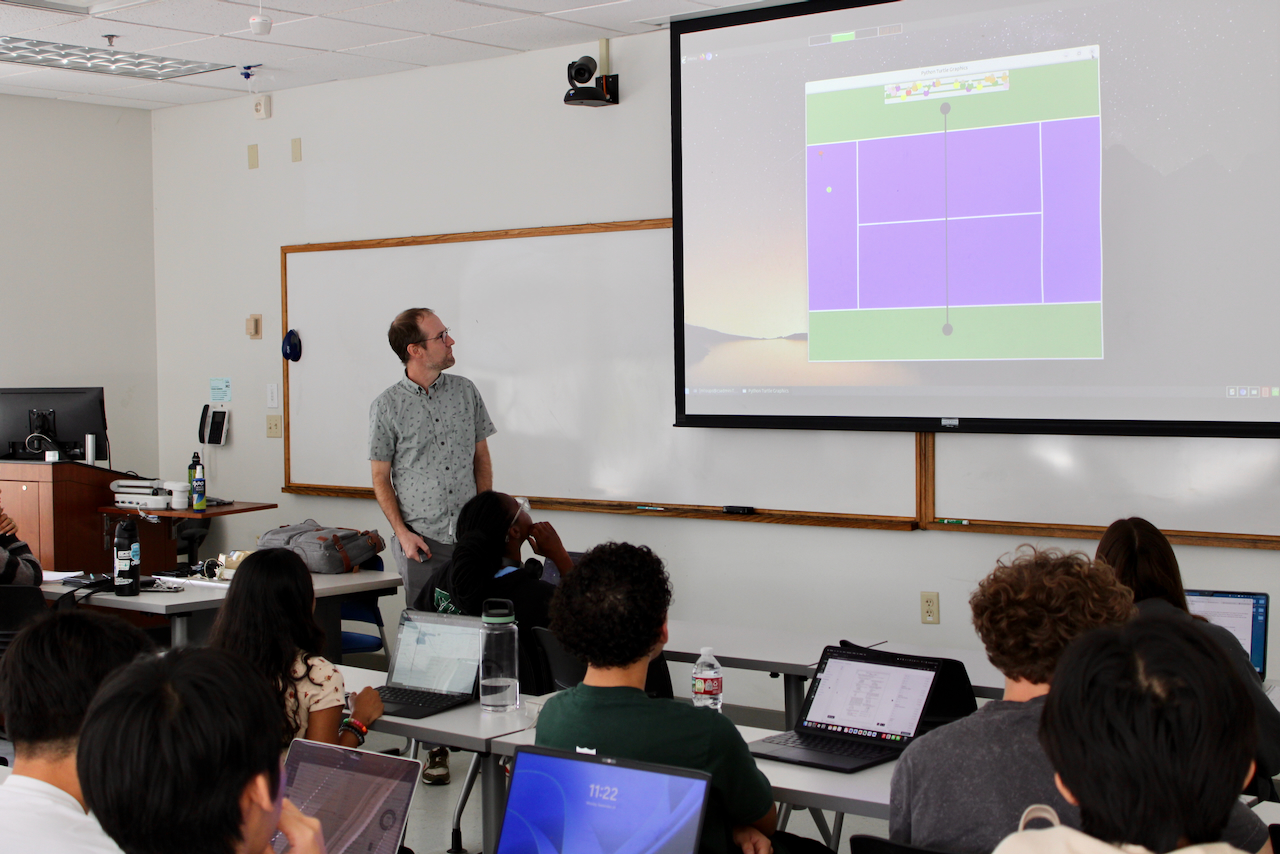 Man presents a video game on a projector screen to an audience.