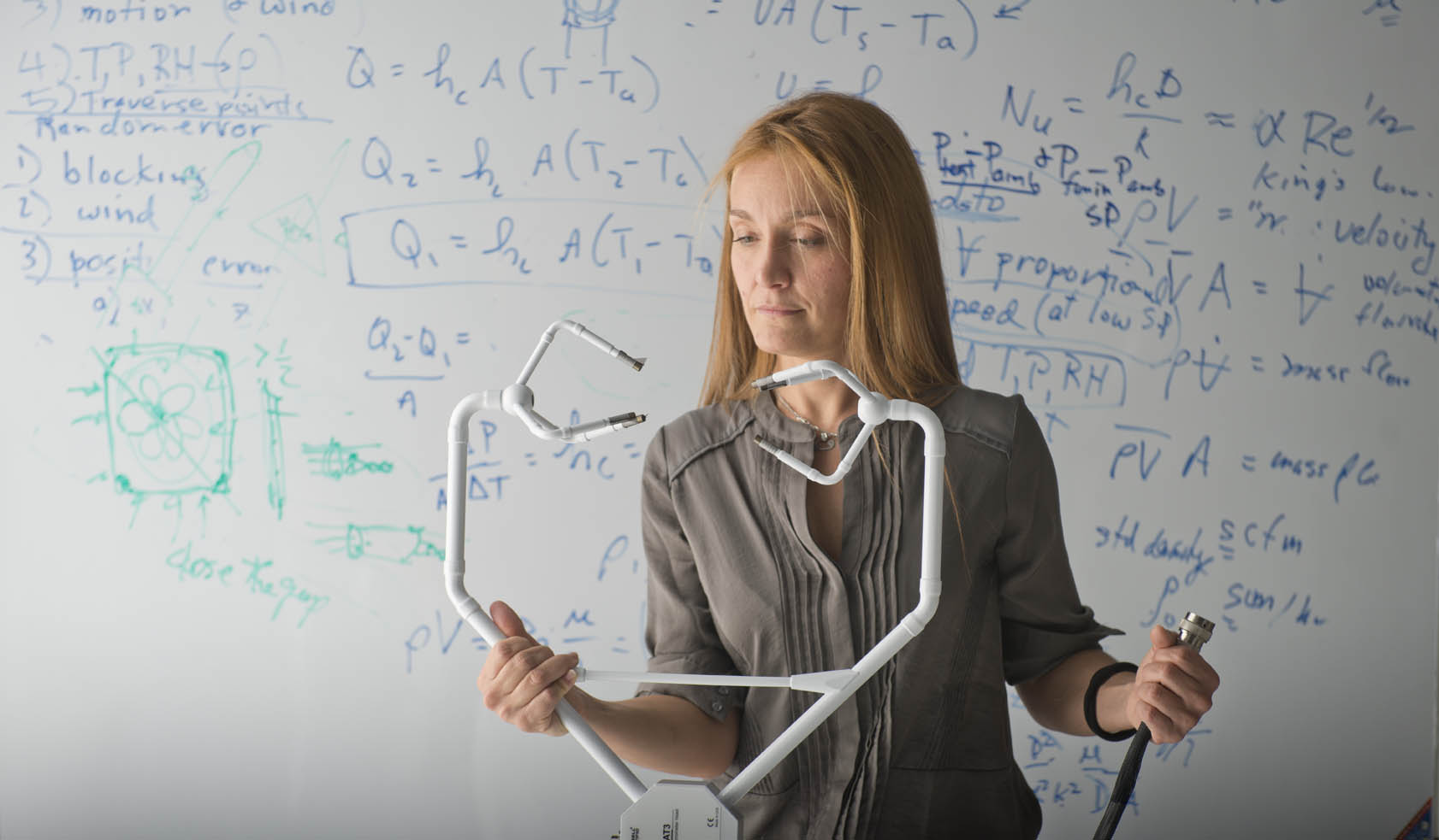 A woman holds a stethoscope in front of a whiteboard covered in equations.