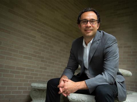 Man in suit and glasses smiles, sitting on stone steps.