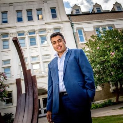 Man in blue suit smiling in front of a building.