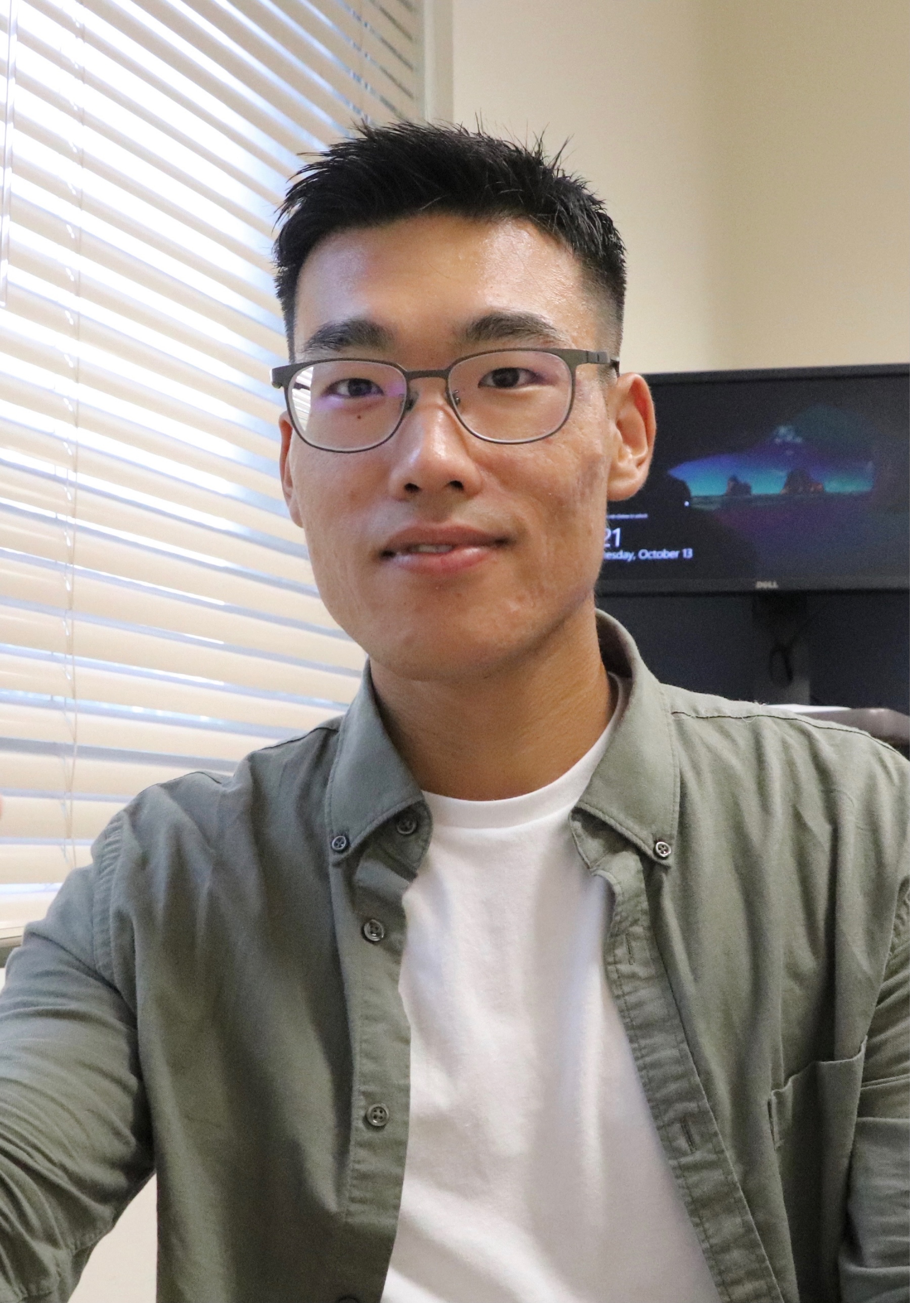 Young Asian man with glasses smiles at the camera.