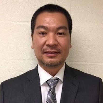 Headshot of man in black suit and tie looking at camera
